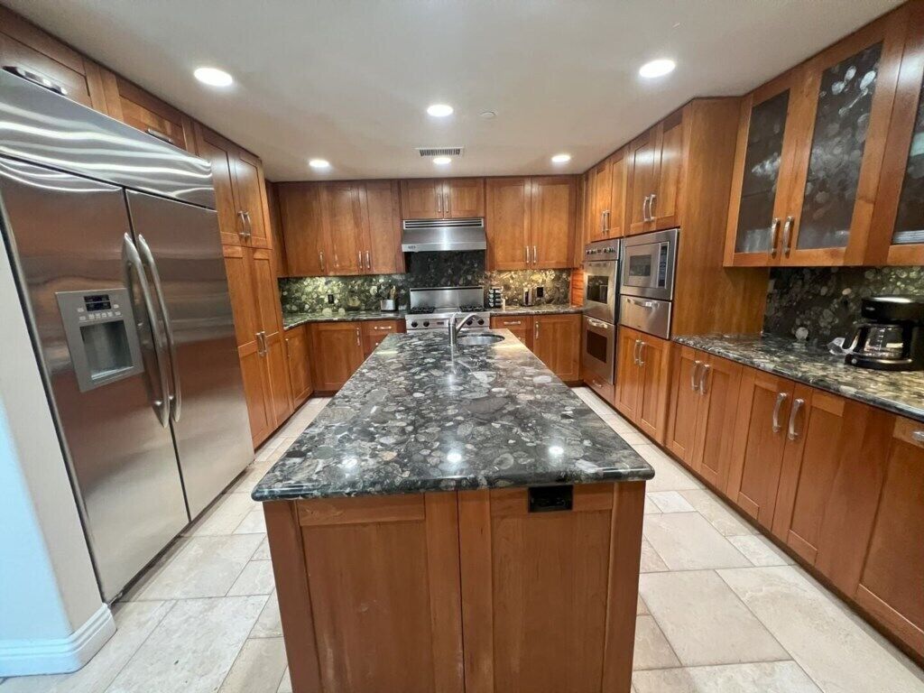 A modern kitchen with wooden cabinets, stainless steel appliances, and a granite countertop.