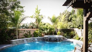 A swimming pool with a waterfall feature, surrounded by lush greenery and a pergola structure. - Fantastic 5 Bedroom 4 Bath Home With new Pool & Jacuzzi (Anaheim)