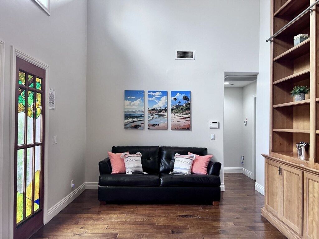 Un salon avec un canapé en cuir noir, un plancher en bois et un meuble en bois doté d’étagères.