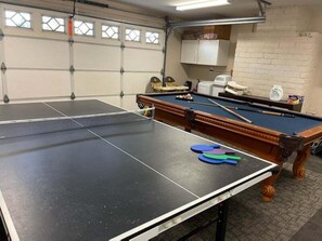 A billiards table with a pool cue and balls, a white cabinet, and a brick wall.