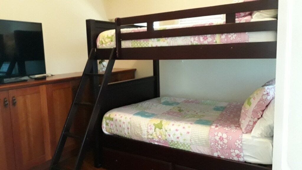 Un lit superposé avec un téléviseur posé sur une commode en bois, une échelle et une couvre-lit à motifs floraux.
