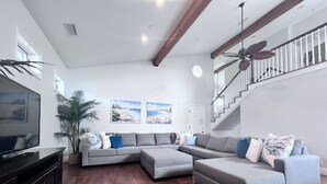 A living room with a sectional sofa, a TV, a ceiling fan, and a staircase. - Fantastic 5 Bedroom 4 Bath Home With new Pool & Jacuzzi (Anaheim)