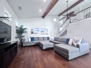 A living room with a sectional sofa, a TV, a ceiling fan, and a staircase.