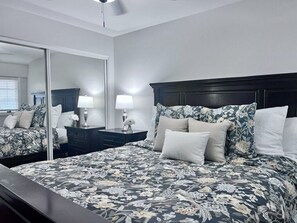 A bedroom with a large bed, a nightstand, a mirror, and a ceiling fan.