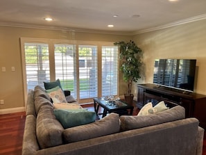 A living room with a sofa, a coffee table, a television, and a large window with blinds. - Amazing Large Family Home W/pool, 1 Mile to Disney (Anaheim)
