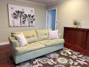 A living room with a green sofa, a floral rug, a framed picture on the wall, and a wooden cabinet. - Amazing Large Family Home W/pool, 1 Mile to Disney (Anaheim)