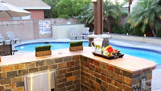 A poolside bar with a stone countertop, a small refrigerator, and a decorative flower arrangement. - Amazing Large Family Home W/pool, 1 Mile to Disney (Anaheim)