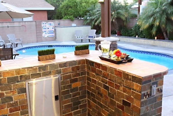Eine Poolbar mit einer Steintheke, einem kleinen Kühlschrank und einer dekorativen Blumenkomposition.