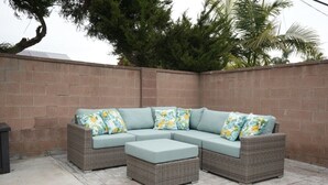 A sectional sofa with floral cushions, a matching ottoman, and a brick wall backdrop. - Amazing Large Family Home W/pool, 1 Mile to Disney (Anaheim)