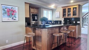 A kitchen with wooden cabinets, a central island with stools, a large window, and a staircase in the background. - Amazing Large Family Home W/pool, 1 Mile to Disney (Anaheim)