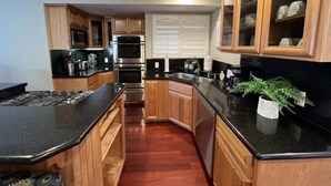 A kitchen with wooden cabinets, a black countertop, stainless steel appliances, and a potted plant. - Amazing Large Family Home W/pool, 1 Mile to Disney (Anaheim)