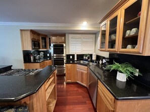 A kitchen with wooden cabinets, a black countertop, stainless steel appliances, and a potted plant. - Amazing Large Family Home W/pool, 1 Mile to Disney (Anaheim)