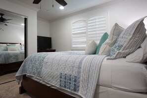 A bedroom with a bed, a TV, a ceiling fan, and a window with blinds.