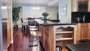 A kitchen with wooden cabinets, a black countertop, a stainless steel refrigerator, and a dining area with a table and chairs. - Amazing Large Family Home W/pool, 1 Mile to Disney (Anaheim)