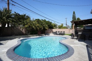 A swimming pool with a curved edge, surrounded by a concrete deck and lounge chairs.