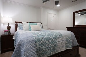A bedroom with a bed, a nightstand, a dresser, a ceiling fan, and a door.