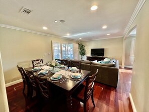 A dining area with a table set for four, a sofa, and a television in the background.