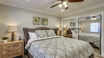 Un dormitorio con cama, mesitas de noche, ventilador de techo y un espejo grande.