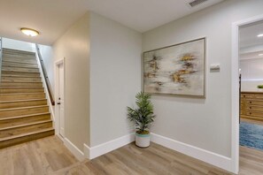 Un pasillo con una escalera de madera, una planta en maceta y un cuadro abstracto enmarcado en la pared.