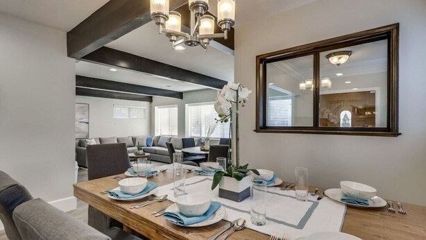 Un coin repas avec une table en bois dressée pour quatre personnes, un lustre et un grand miroir au mur.