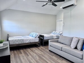 A modern bedroom with two beds, a sofa, a ceiling fan, and an air conditioning unit. - 5 Bedroom plus loft room, 3 Bath home (Fullerton)