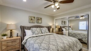 Une chambre à coucher avec un lit, des tables de chevet, un ventilateur de plafond et un grand miroir.