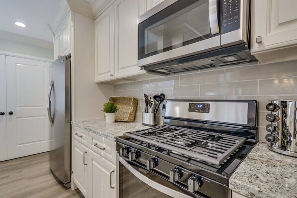 A modern kitchen with white cabinetry, a stainless steel refrigerator, a built-in microwave, and a gas stove.