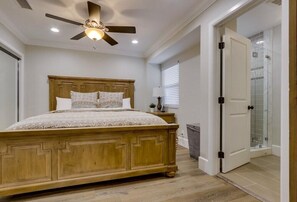 Ein Schlafzimmer mit einem hölzernen Bett, einem Deckenventilator, einem Nachttisch und einem Badezimmer mit einer Duschkabine.