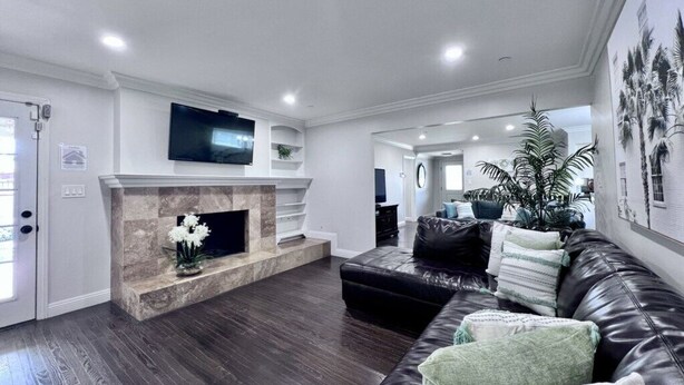 A modern living room with a fireplace, a black leather sofa, and a television mounted on the wall. - Dazzling 5 Bedroom Pool Home 1/4 Mile To Disney (Anaheim)