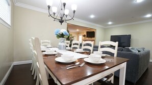 A dining area with a wooden table, white chairs, and a chandelier. - Dazzling 5 Bedroom Pool Home 1/4 Mile To Disney (Anaheim)