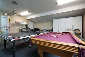 A billiards table with a TIGA logo, a pool table, and a white cabinet in a room with beige walls and a ceiling fan.
