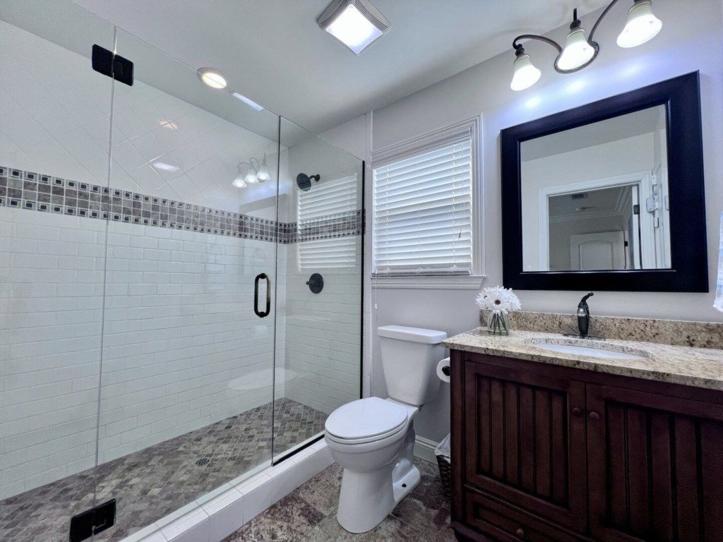 A bathroom with a glass shower enclosure, a toilet, a vanity with a mirror, and a sink.