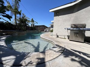 A swimming pool with a curved edge, a barbecue grill, and a stone wall. - Dazzling 5 Bedroom Pool Home 1/4 Mile To Disney (Anaheim)