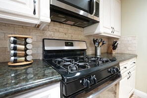 A kitchen with a black stove, white cabinets, a microwave, and a spice rack.