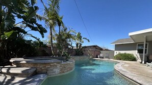 A swimming pool with a curved design, surrounded by stone steps and tropical plants. - Dazzling 5 Bedroom Pool Home 1/4 Mile To Disney (Anaheim)
