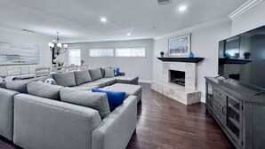 A living room with a sectional sofa, a fireplace, a television, and a dining area with a table and chairs. - Awesome Pool Home 1/4 Mile To Disney Tram on Magic Way (Anaheim)