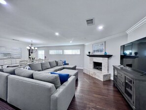 A living room with a sectional sofa, a fireplace, a television, and a dining area with a table and chairs. - Awesome Pool Home 1/4 Mile To Disney Tram on Magic Way (Anaheim)