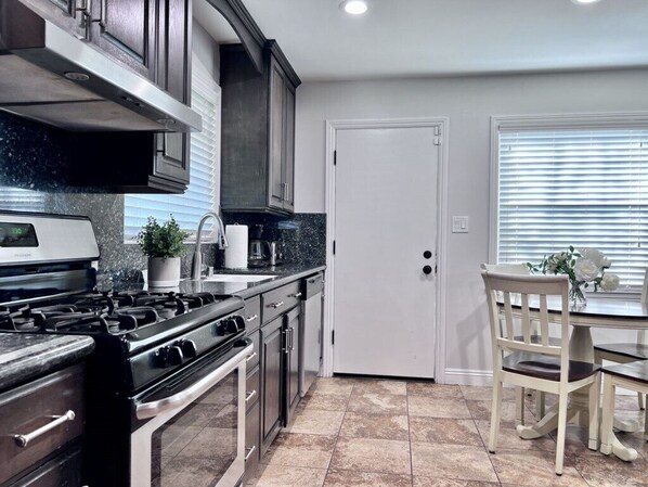 A kitchen with a stove, oven, cabinets, and a dining area with a table and chairs. - Awesome Pool Home 1/4 Mile To Disney Tram on Magic Way (Anaheim)