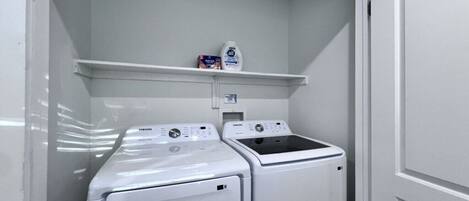 A laundry room with two front-loading washers and dryers, a shelf with detergent, and a control panel.