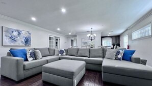 A modern living room with a sectional sofa, ottoman, and a chandelier. - Awesome Pool Home 1/4 Mile To Disney Tram on Magic Way (Anaheim)