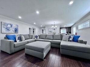 A modern living room with a sectional sofa, ottoman, and a chandelier. - Awesome Pool Home 1/4 Mile To Disney Tram on Magic Way (Anaheim)