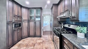 A kitchen with dark wood cabinets, a stainless steel range hood, a microwave, and a granite countertop. - Awesome Pool Home 1/4 Mile To Disney Tram on Magic Way (Anaheim)