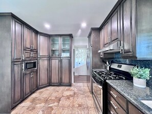 A kitchen with dark wood cabinets, a stainless steel range hood, a microwave, and a granite countertop. - Awesome Pool Home 1/4 Mile To Disney Tram on Magic Way (Anaheim)
