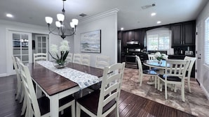 A dining area with a wooden table, white chairs, and a chandelier. - Awesome Pool Home 1/4 Mile To Disney Tram on Magic Way (Anaheim)