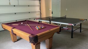 A pool table with a cue stick and balls, a ping pong table, and a garage door in the background. - Awesome Pool Home 1/4 Mile To Disney Tram on Magic Way (Anaheim)
