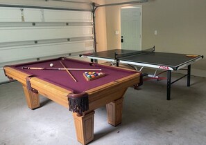 A pool table with a cue stick and balls, a ping pong table, and a garage door in the background. - Awesome Pool Home 1/4 Mile To Disney Tram on Magic Way (Anaheim)