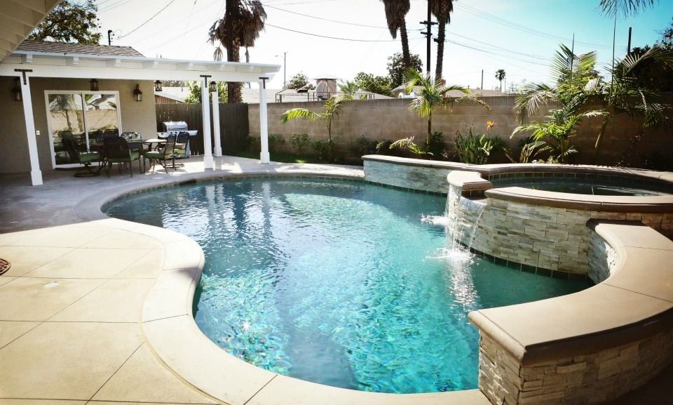 A swimming pool with a stone waterfall feature, surrounded by a patio area with outdoor furniture.