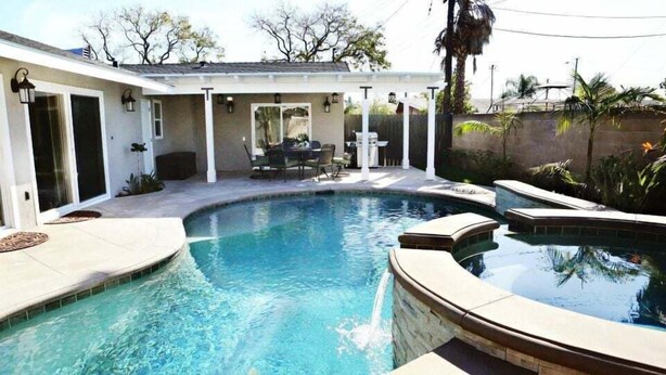 A swimming pool with a curved edge, surrounded by a covered patio area with outdoor furniture. - Fantastic 6 bedroom, 4.5 bath home (4 master Suites), pool home (Anaheim)