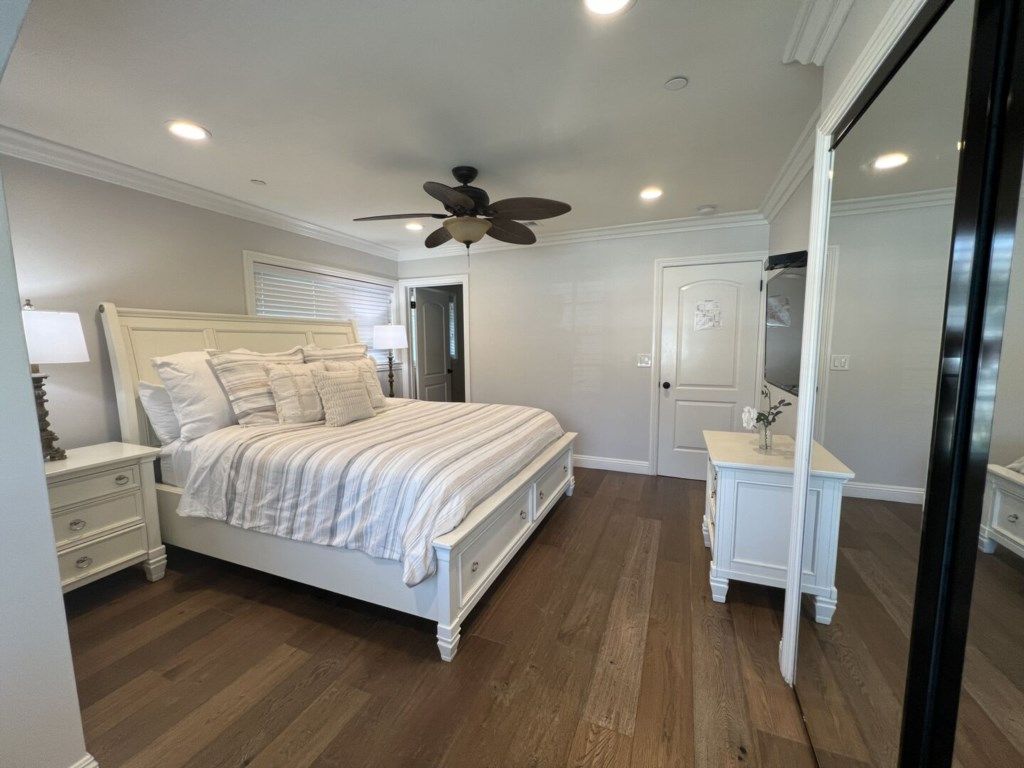 Un dormitorio con cama, mesitas de noche, cómoda, ventilador de techo y una puerta.