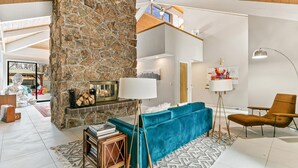 Uma sala de estar moderna com lareira de pedra, um sofá verde-água, uma poltrona marrom e uma janela grande.